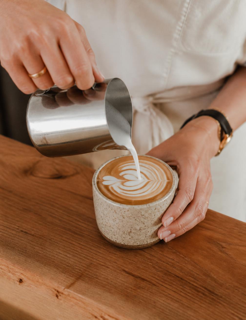 Barista pouring latte art into a ceramic cup